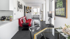 En moderne stue med en rød sofa, et glasbord og et stort abstrakt billede på væggen.