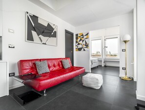 A modern living room with a red leather sofa, a white ottoman, and abstract wall art. - Porta Nuova 52 Design Apartment R&R (Milan)