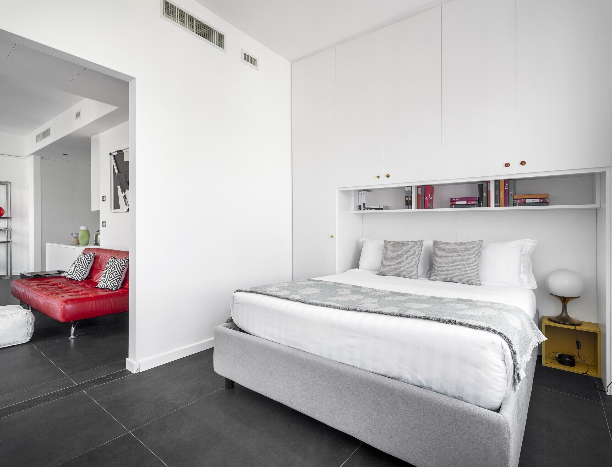 A modern bedroom with a bed, a red sofa, and a white wardrobe.