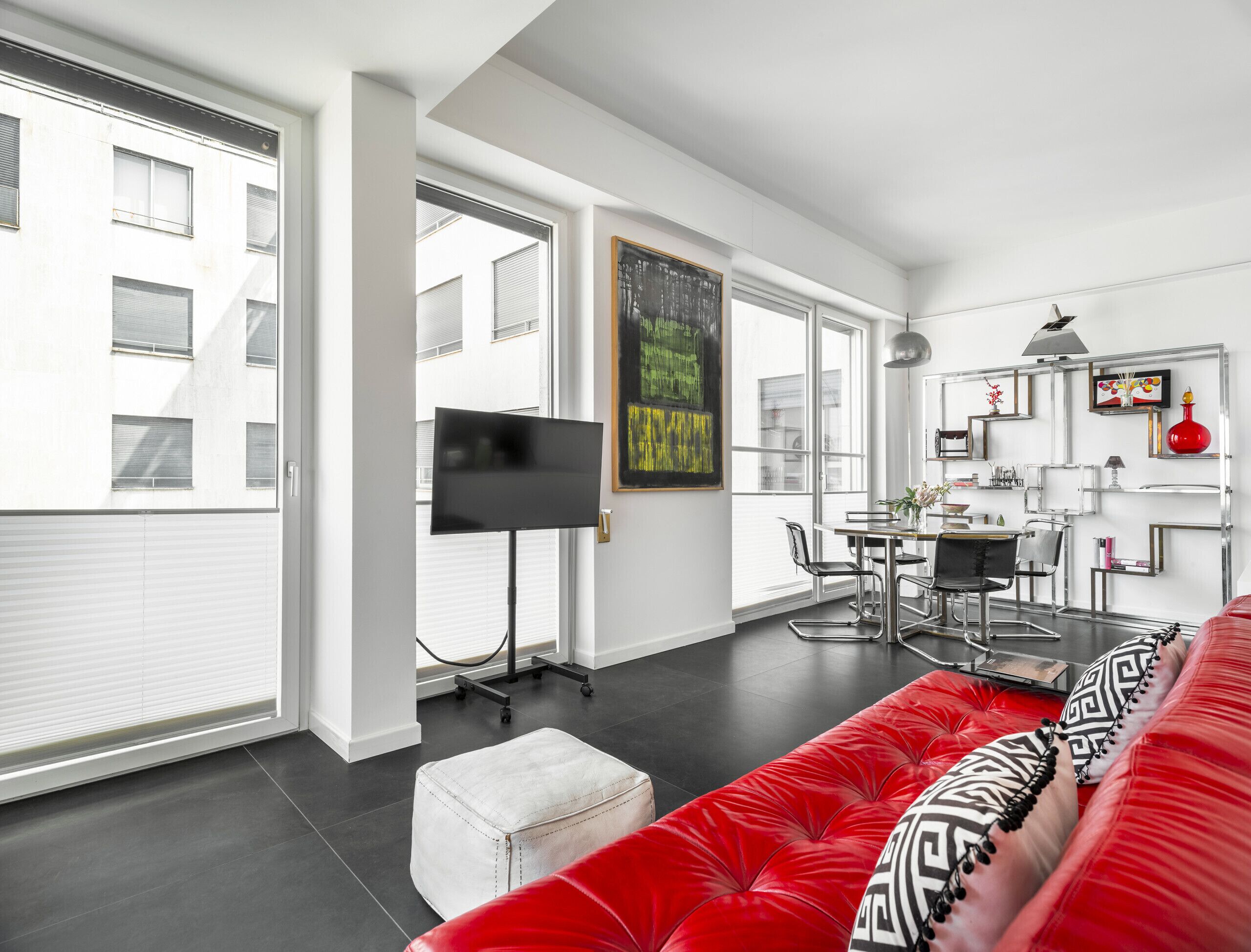A modern living room with a red sofa, a flat-screen TV, and a dining area with a table and chairs.