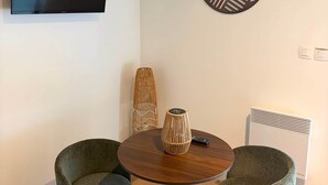 A room with a round wooden table, two upholstered chairs, a television mounted on the wall, a decorative wall piece, and a radiator. - L'Évidence - Love Room & Spa (Chaveignes)