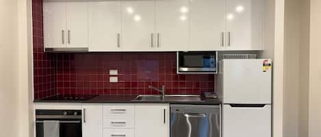 Una cocina compacta con armarios blancos, microondas, lavavajillas y refrigerador.