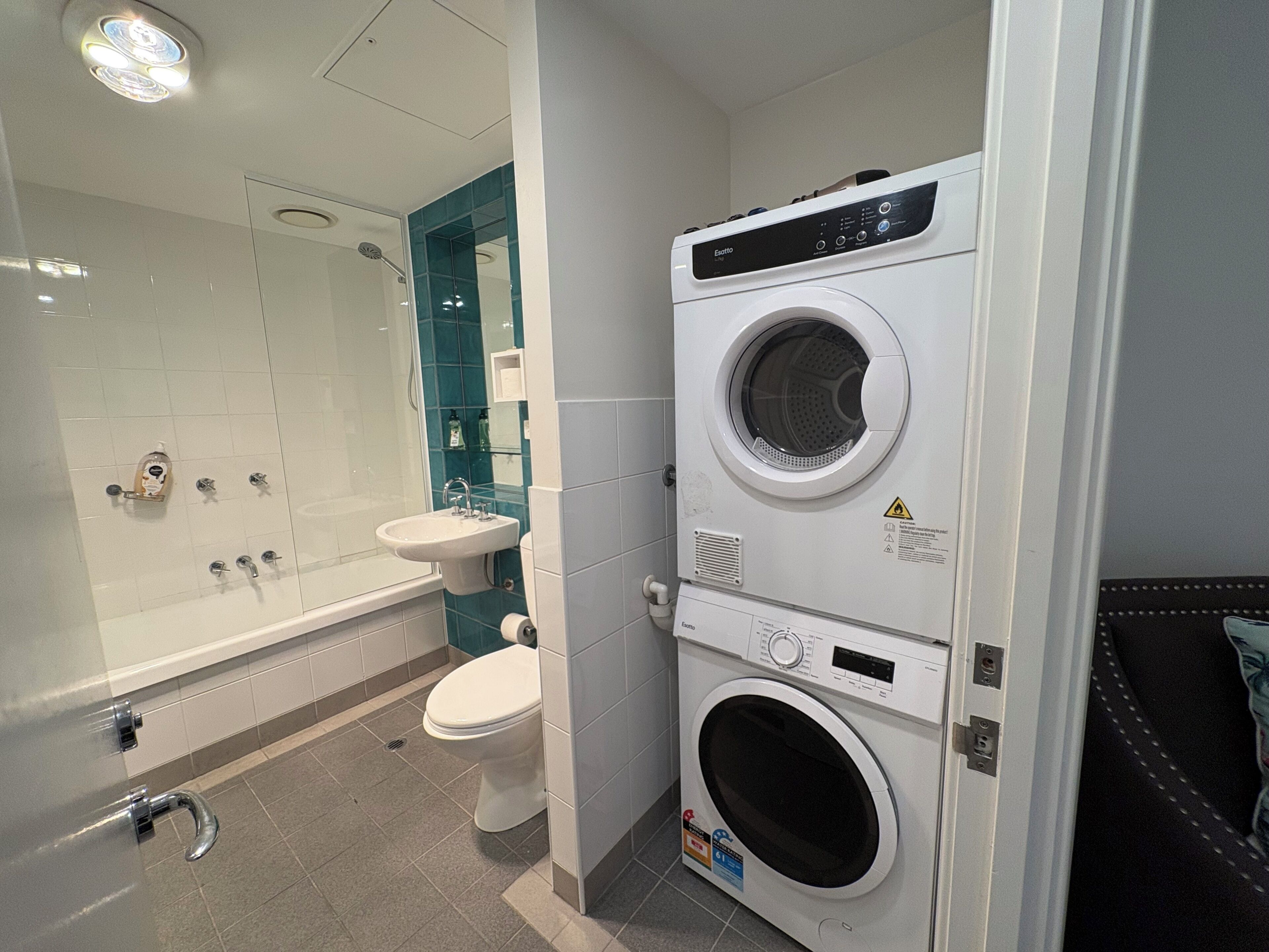 A compact bathroom with a built-in washing machine, a glass shower enclosure, and a sink.
