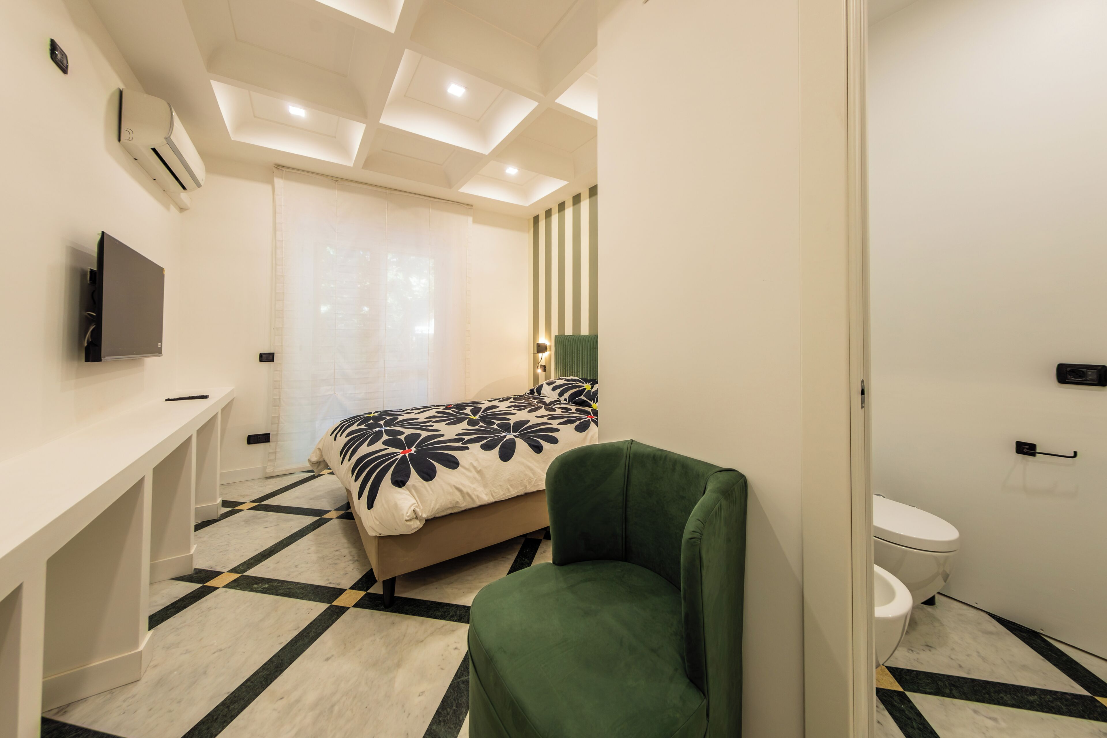 Een moderne slaapkamer met een bed, een groene stoel, een bureau, een televisie en een badkamer.