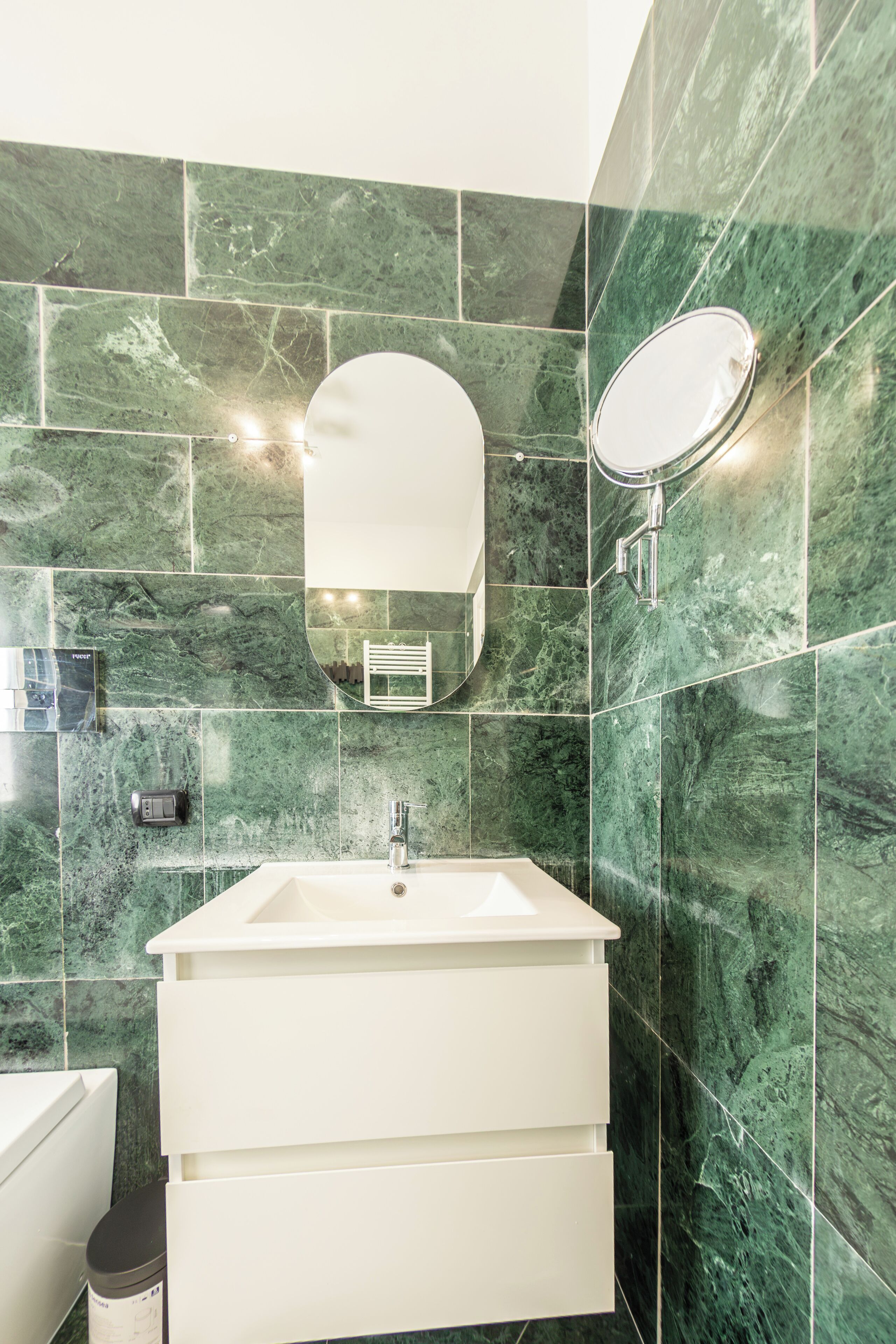 A bathroom with a white sink, a mirror, and green marble tiles.