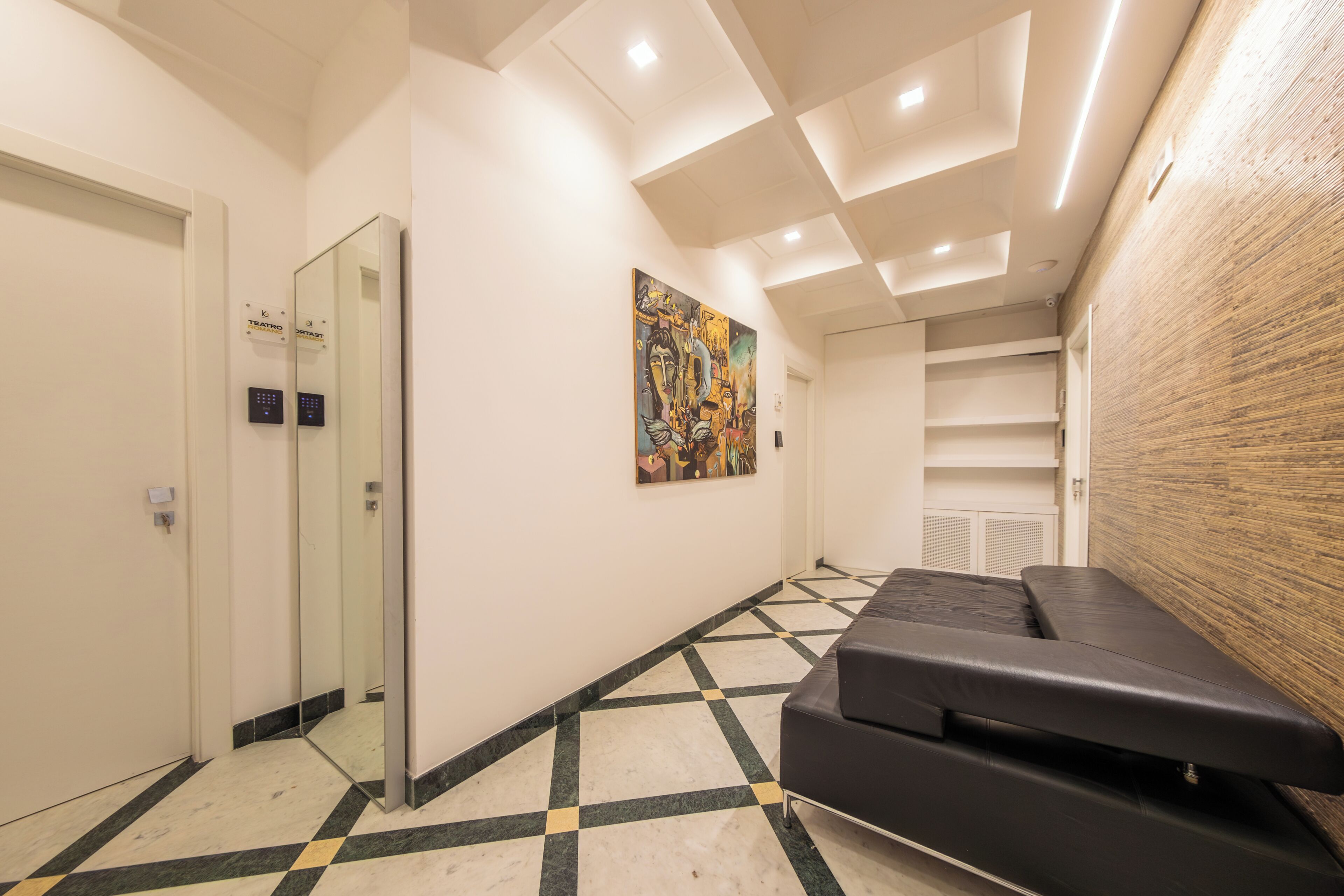 A hallway with a checkered floor, a black sofa, a painting, and an elevator.