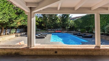 Una piscina exterior techada con sillas de descanso y un sofá rojo.