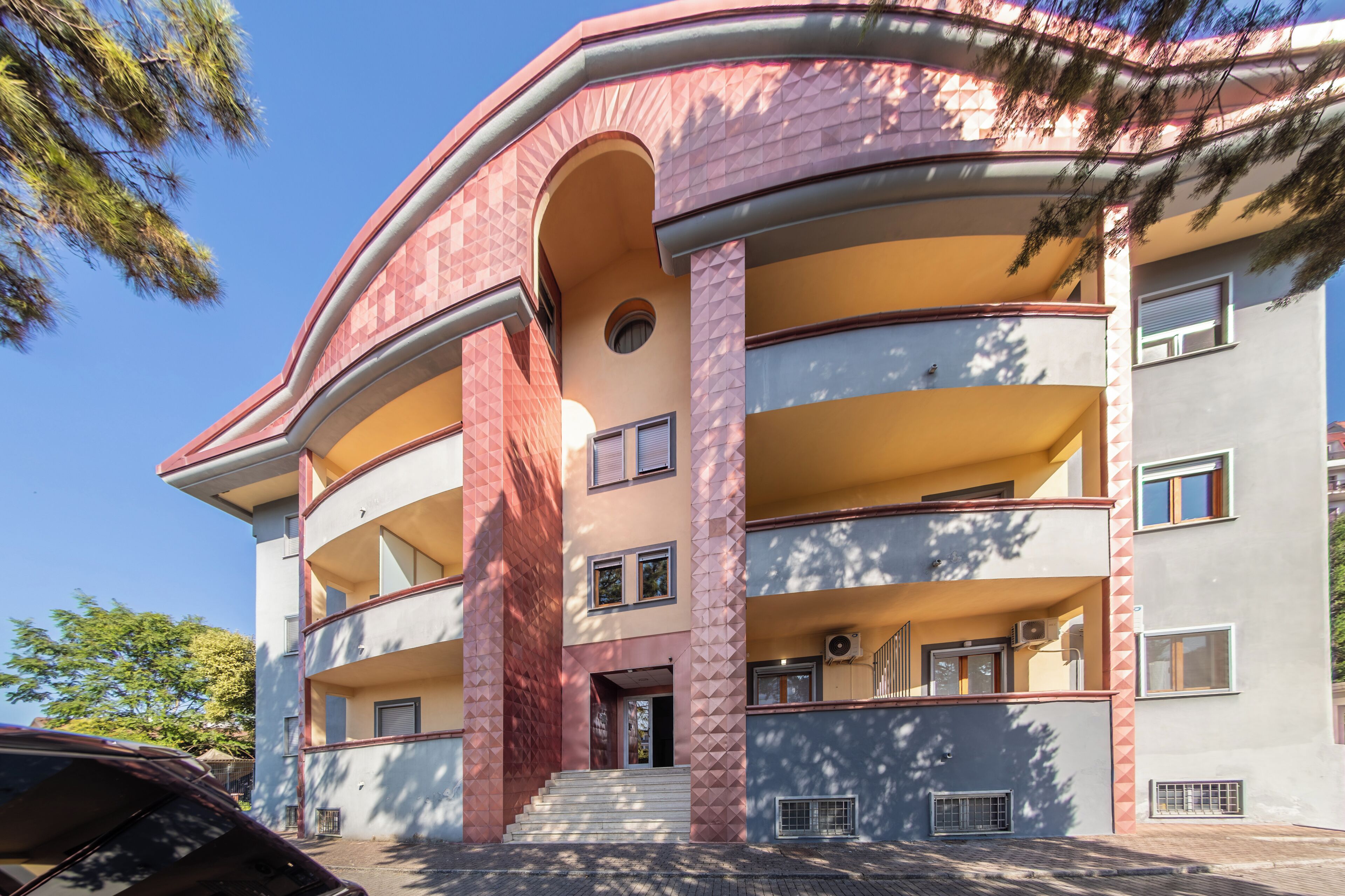 Ein mehrgeschossiges Gebäude mit einer gewölbten Fassade, Balkonen und einem zentralen Eingang.