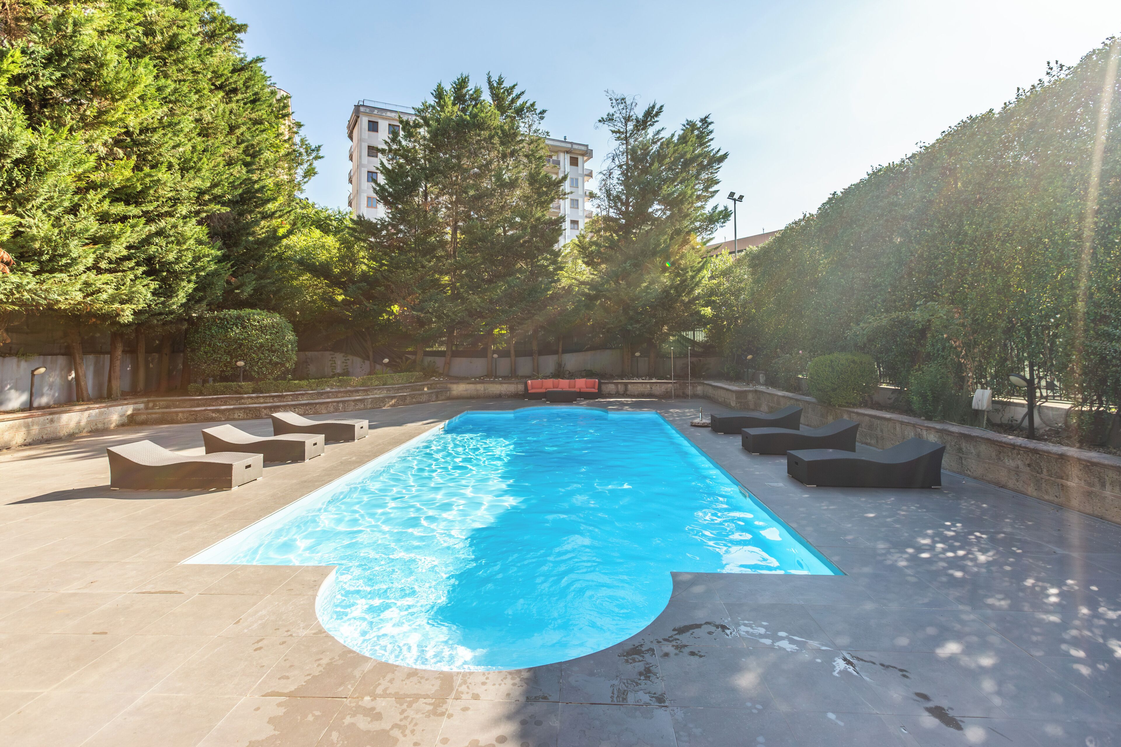 A rectangular swimming pool with a curved edge, surrounded by lounge chairs and a low wall.
