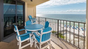 A balcony with a table and chairs, overlooking a beach with umbrellas and people. - Phoenix Iii 3071 3 Bedroom Condo (Orange Beach)