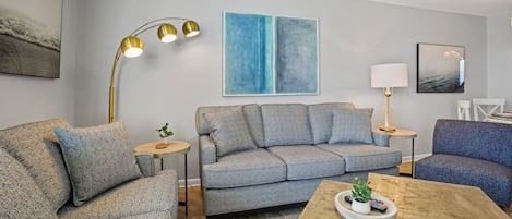 Una sala de estar moderna con un sofá gris, una mesa de centro de madera y una lámpara de pie.