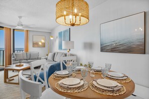 Ein modernes Wohnzimmer mit Essbereich für vier Personen, ausgestattet mit einem runden Tisch, einer gewebten Tischunterlage, weißen Tellern und klaren Gläsern.