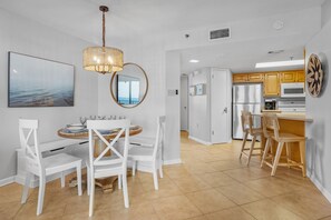 Una cocina moderna con armarios blancos, un comedor con sillas blancas y un amplio ventanal con vistas al mar.