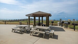 Un área de picnic techada con mesas, bancos, una parrilla y vista a la playa.
