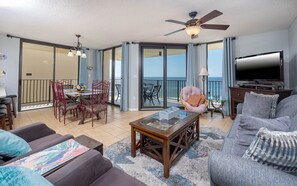 A spacious living area with a balcony, a television, and a dining set. - Phoenix Iv 4085 3 Bedroom Condo (Orange Beach)