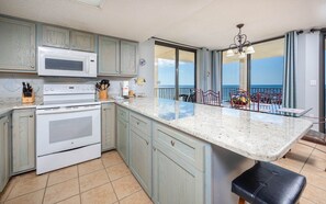 A kitchen with a large island, a microwave, an oven, and a dining area with a view. - Phoenix Iv 4085 3 Bedroom Condo (Orange Beach)