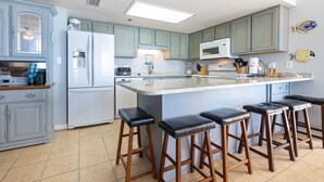 A kitchen with a central island, bar stools, and a fish decoration on the wall. - Phoenix Iv 4085 3 Bedroom Condo (Orange Beach)