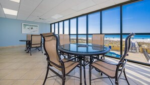 A conference room with a glass table and chairs, large windows with a beach view, and a tiled floor. - Phoenix Iv 4085 3 Bedroom Condo (Orange Beach)