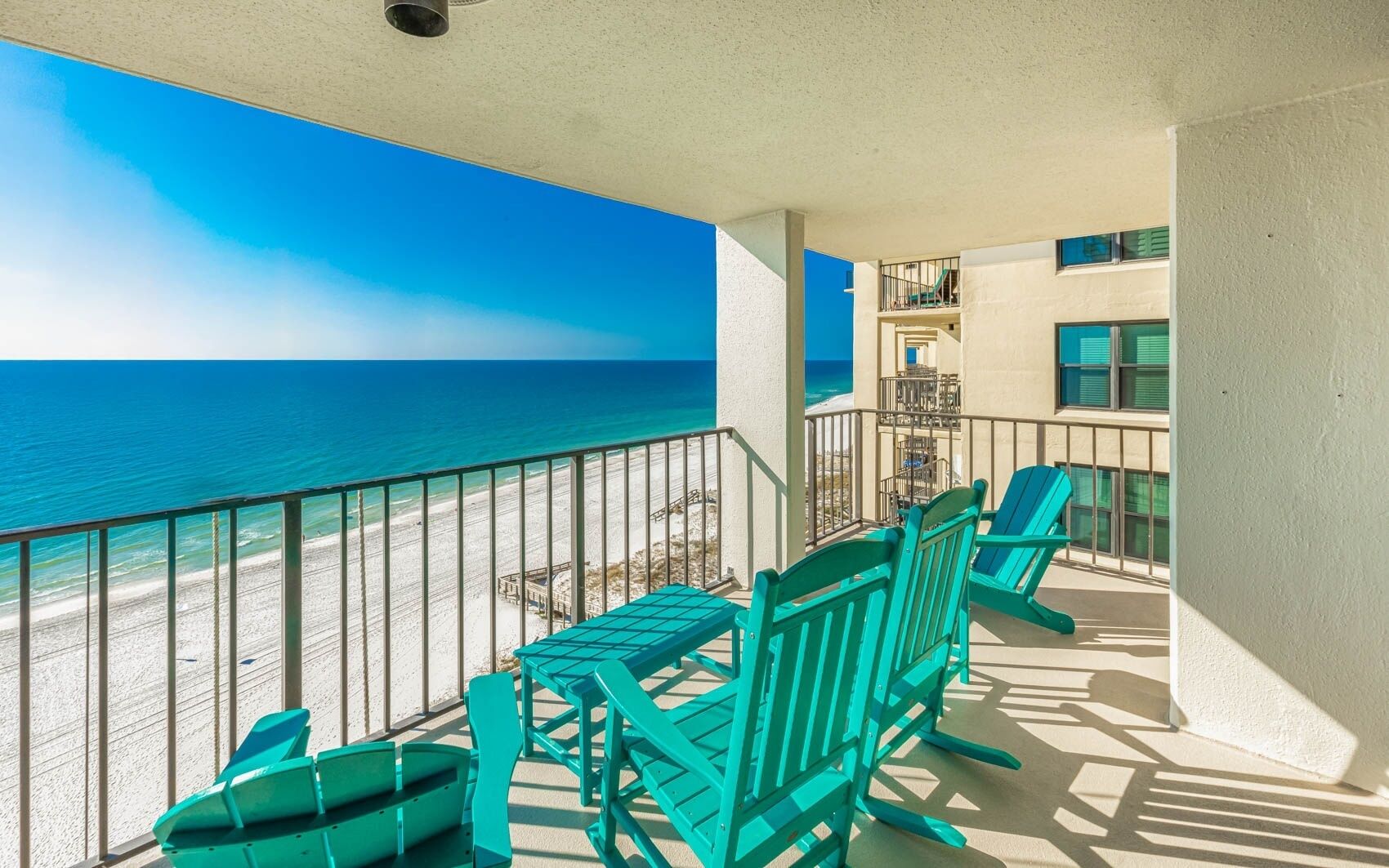 A balcony with a view of the beach and ocean. There are green chairs and a table.