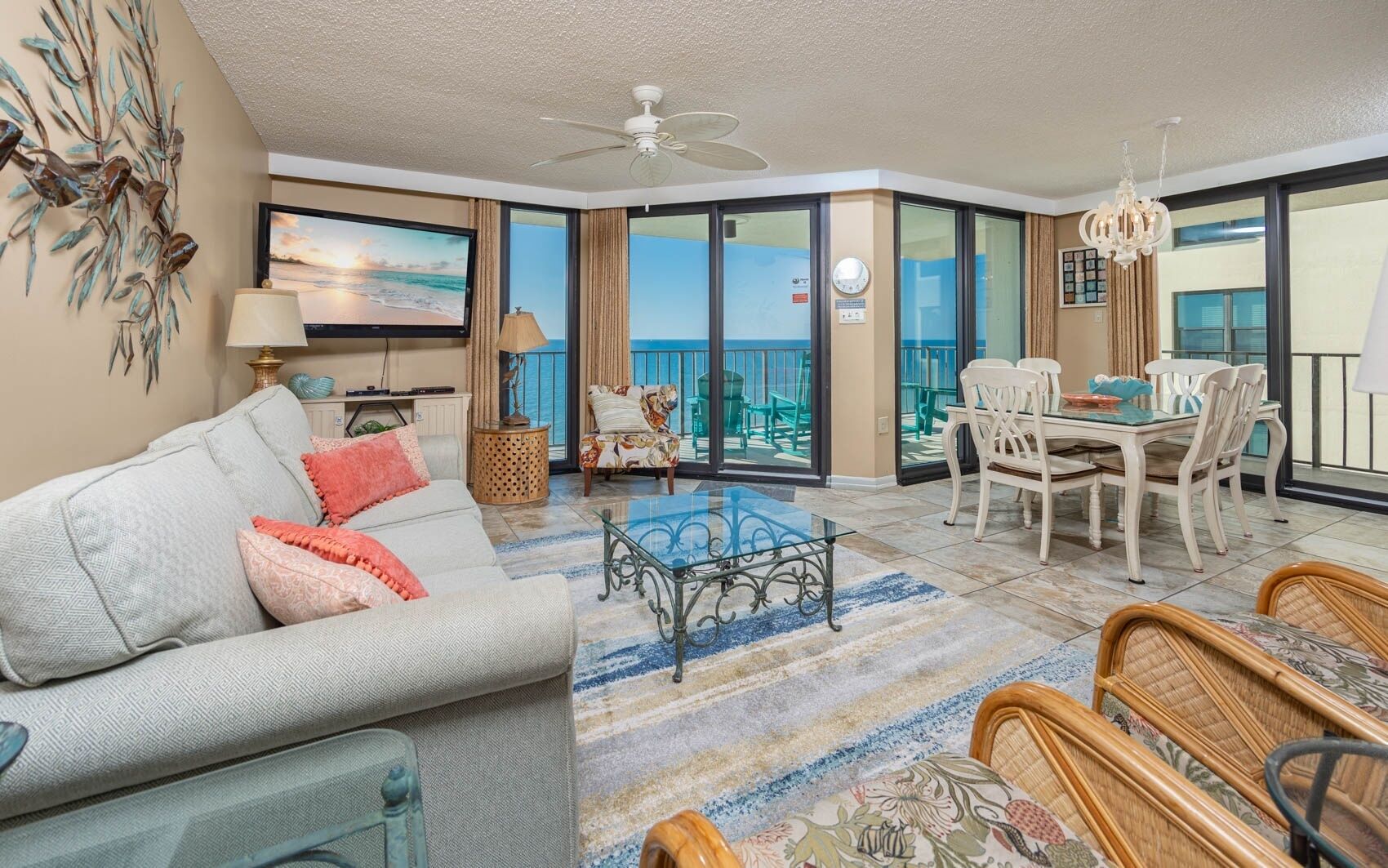 A spacious living area with a sofa, coffee table, and dining set. There is a balcony with a view of the ocean.