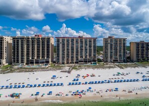 Ett hotell vid stranden med flera höga byggnader, en sandstrand med parasoller och en klar himmel.