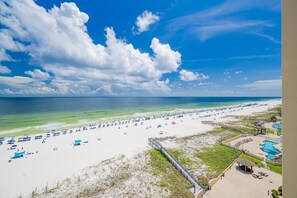 A beach with a clear sky, a sandy shore, and a pool area with a wooden deck. - Phoenix Iii 3098 2 Bedroom Condo (Orange Beach)
