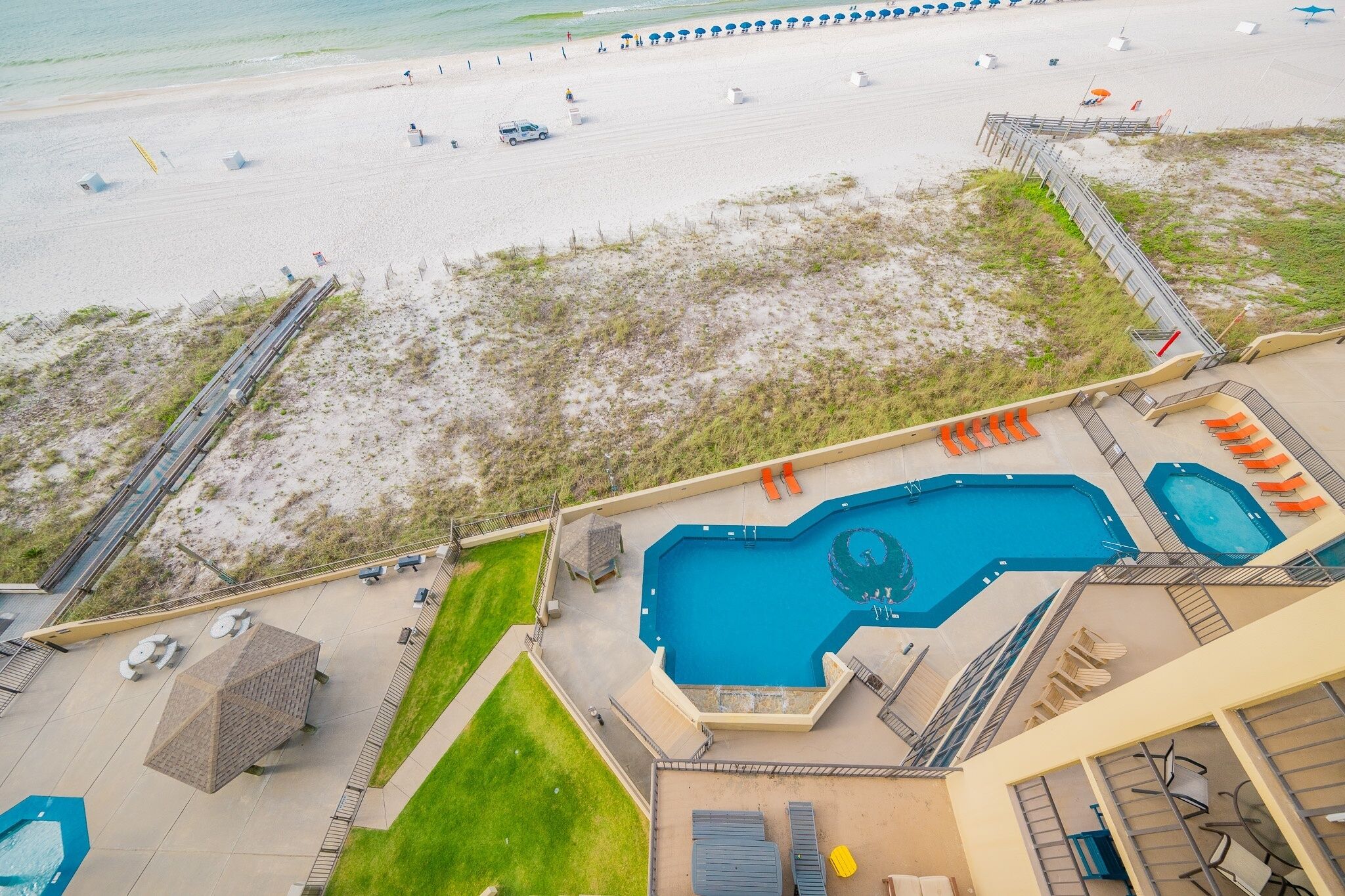A pool area with multiple pools and lounge chairs, surrounded by a sandy beach and a grassy area.