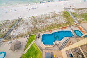 Ein Poolbereich mit mehreren Pools und Liegestühlen, umgeben von einem Sandstrand und einer Rasenfläche.