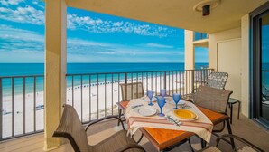 Ein Balkon mit Tisch für zwei Personen, mit Blick auf einen Strand mit Sonnenschirmen und einem wolkenlosen Himmel.