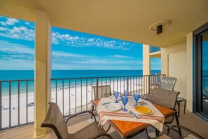 A balcony with a table set for two, overlooking a beach with umbrellas and a clear sky. - Phoenix Iii 3089 3 Bedroom Condo (Orange Beach)