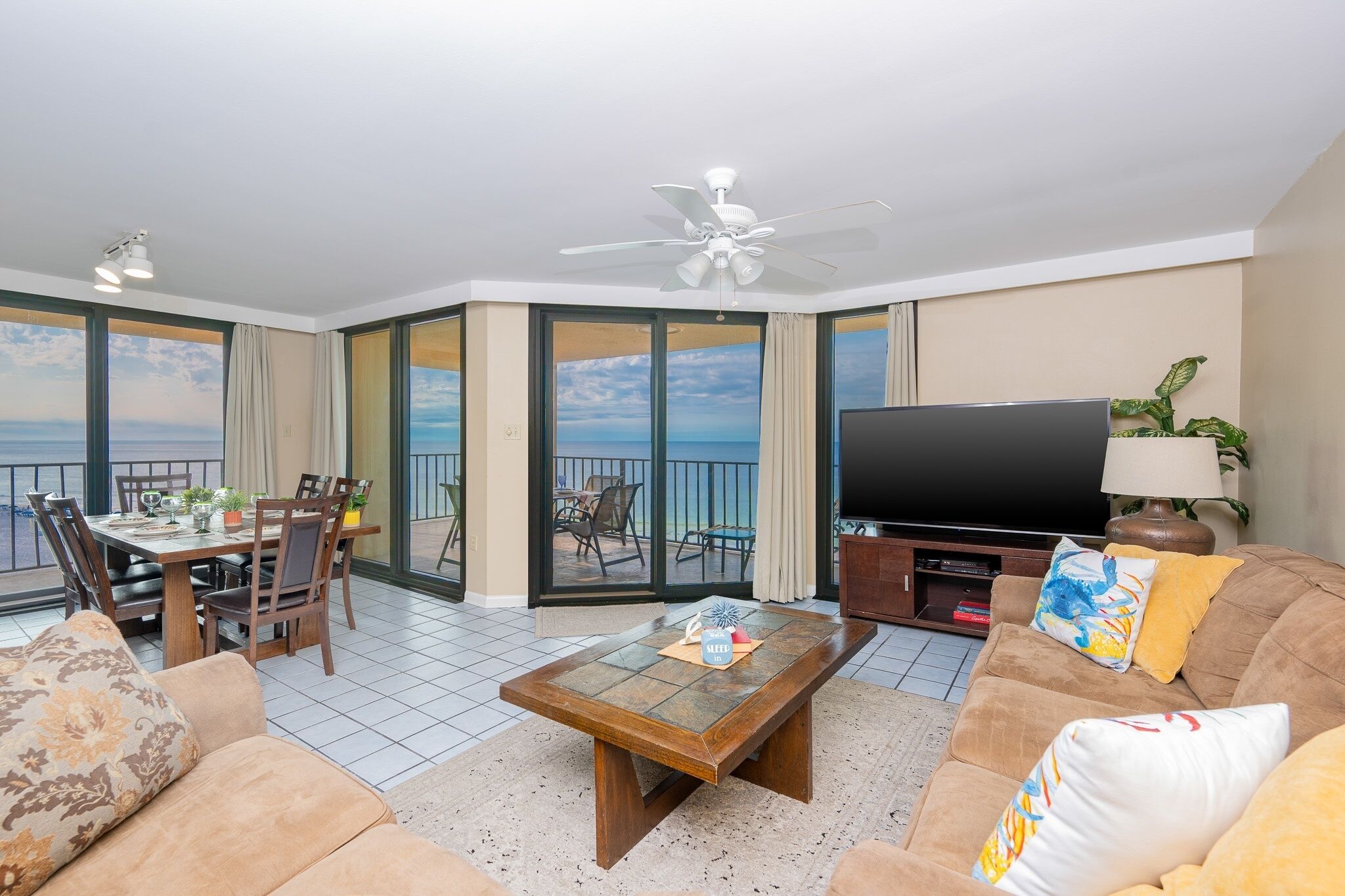 A modern living room with a dining area, a flat-screen TV, and a balcony with a view.