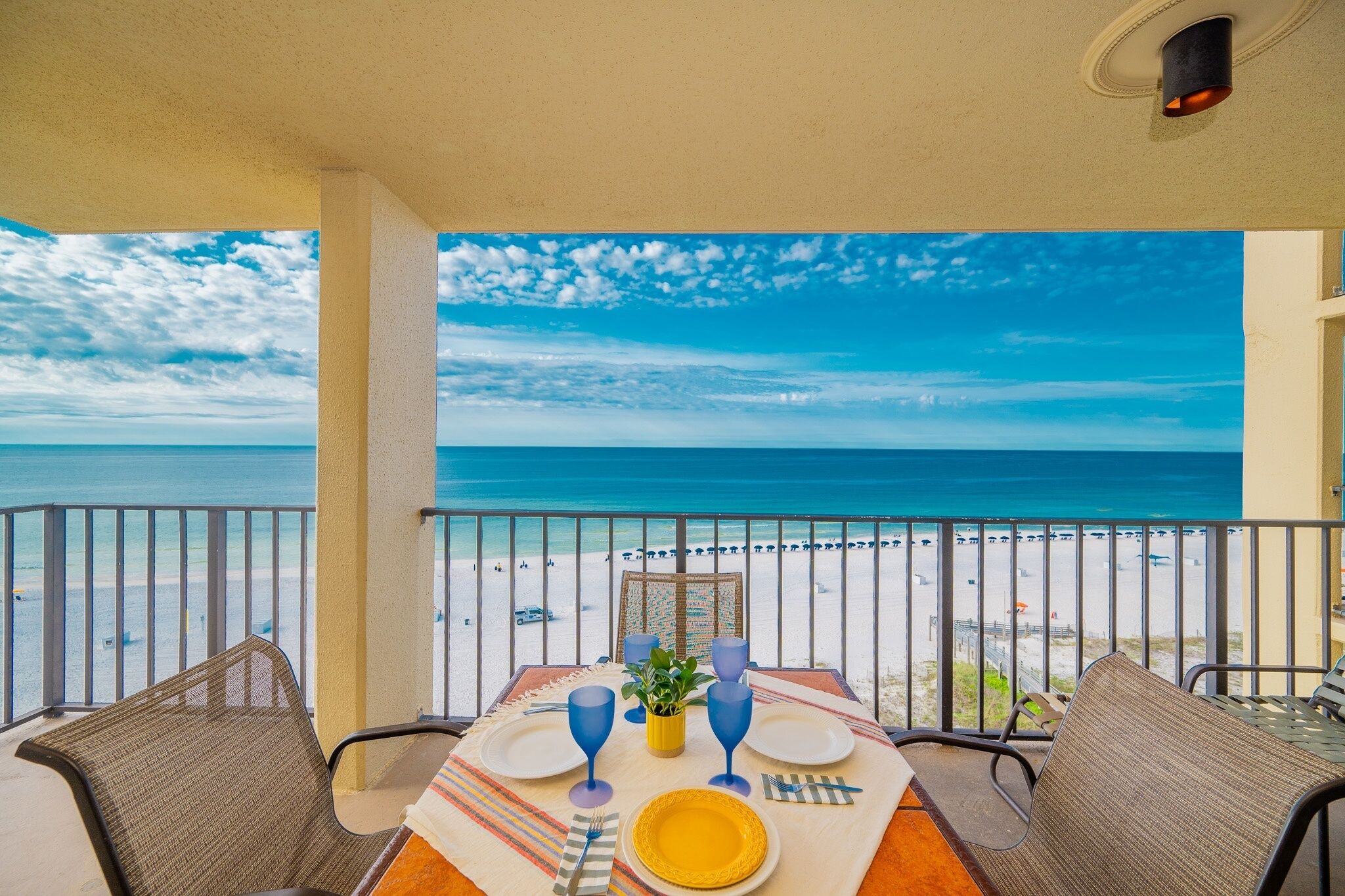 A dining area with a table set for two, overlooking a beach with a clear view of the ocean and sky.