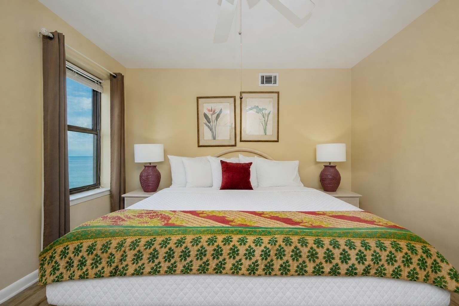 A hotel room with a large bed, two bedside lamps, a window with curtains, and two framed pictures on the wall.
