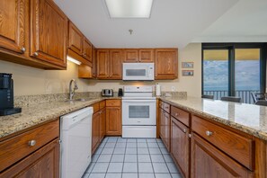 A kitchen with wooden cabinets, a microwave, a stove, and a dishwasher. - Phoenix Iii 3089 3 Bedroom Condo (Orange Beach)