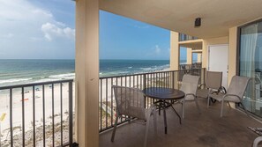 Un balcon avec vue sur la plage et l’océan, aménagé avec des chaises et une table.