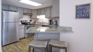 A modern kitchen with a central island, stainless steel appliances, and a bar stool seating area. - Phoenix Iii 3068 2 Bedroom Condo (Orange Beach)