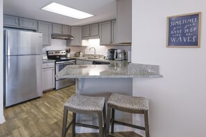 A modern kitchen with a central island, stainless steel appliances, and a bar stool seating area. - Phoenix Iii 3068 2 Bedroom Condo (Orange Beach)