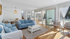 Ein modernes Wohnzimmer mit einem blauen Sofa, weißen Sesseln, einem Couchtisch und einem Essbereich mit Tisch und Stühlen.