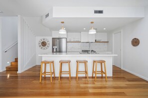 A modern kitchen with a central island, wooden stools, and a stainless steel refrigerator. - 17 Elluisa Close : 4  BR, 3  BA House in Forster, Sleeps 8 (Forster)