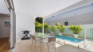 Eine moderne Außenpatio mit einem Glastisch und Stühlen, einem Grill und einem Pool.