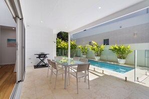 A modern outdoor patio with a glass table and chairs, a barbecue grill, and a pool. - 17 Elluisa Close : 4  BR, 3  BA House in Forster, Sleeps 8 (Forster)