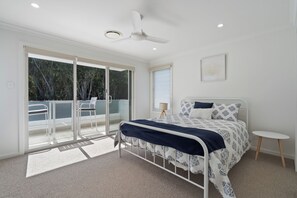 A bedroom with a bed, a ceiling fan, a window with a view of trees, and a door leading to an outdoor area with a table and chairs. - 17 Elluisa Close : 4  BR, 3  BA House in Forster, Sleeps 8 (Forster)