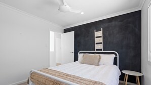 Ein Schlafzimmer mit einem Bett, einem weißen Deckenventilator, einer schwarzen Akzentwand, einem kleinen Nachttisch und einem Fenster.