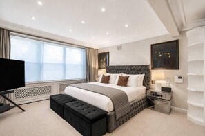 A modern hotel room with a large bed, a flat-screen TV, and a window with curtains. - Luxury Holland Park 3-bed With Private Balcony (London)