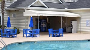 A pool area with blue chairs and umbrellas, a refrigerator, and a Pepsi cooler. - 501l Studio (Calabash)
