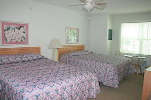 A bedroom with two beds, a ceiling fan, a desk, and a window.