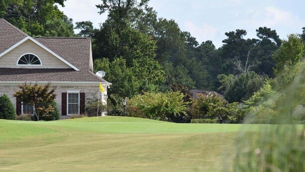 A golf course with a clubhouse and trees in the background. - 501l Studio (Calabash)