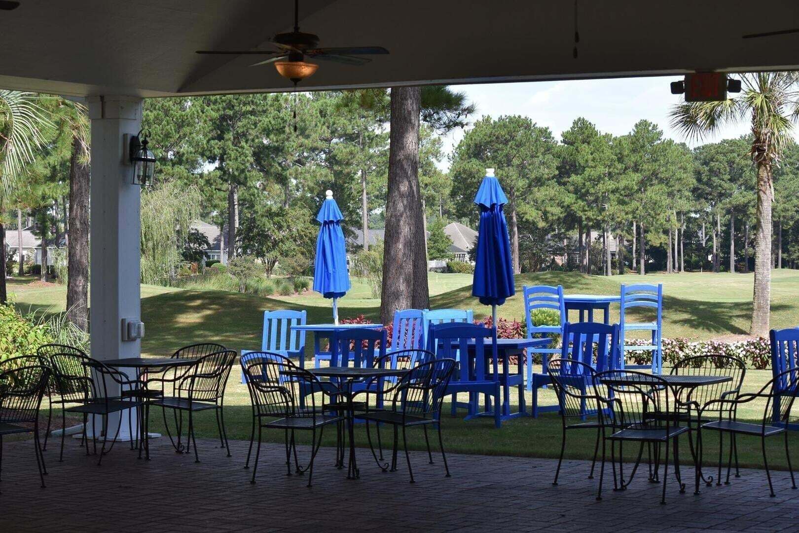 An outdoor patio with blue tables and chairs, umbrellas, and a view of a golf course.