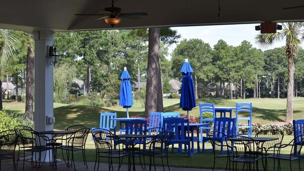 Eine Terrasse im Freien mit blauen Tischen und Stühlen, Sonnenschirmen und Blick auf einen Golfplatz.