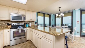 A kitchen with a large island, stainless steel appliances, and a view of the ocean through the windows. - Phoenix East 511 3 Bedroom Condo (Orange Beach)